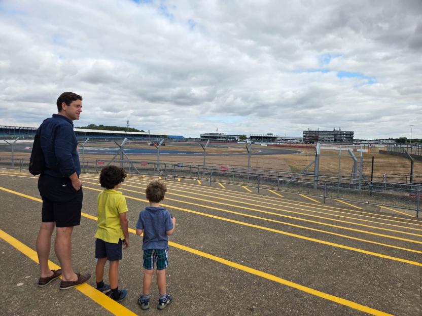 A man and two boys standing on grandstand steps overlooking Silverstone race track.