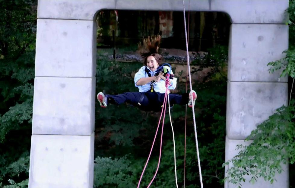 A woman rappelling, mid-air with her legs spread wide, screaming with excitement.