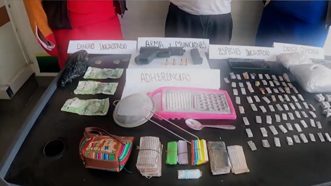A table displaying confiscated money, a handgun and ammunition, a grater, a spoon, a strainer, and numerous small packages of drugs.