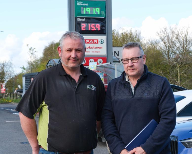 Two hauliers, Kevin Doody and Michael Horan, standing in front of a fuel price sign in Ireland, showing high prices for unleaded and diesel.
