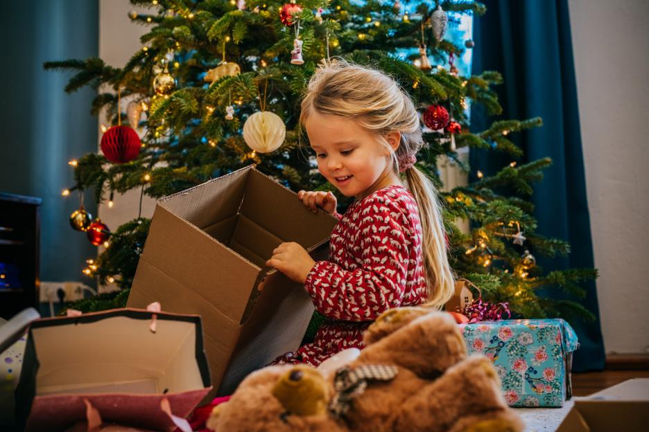Young girl opening Christmas gifts in front of a Christmas tree.