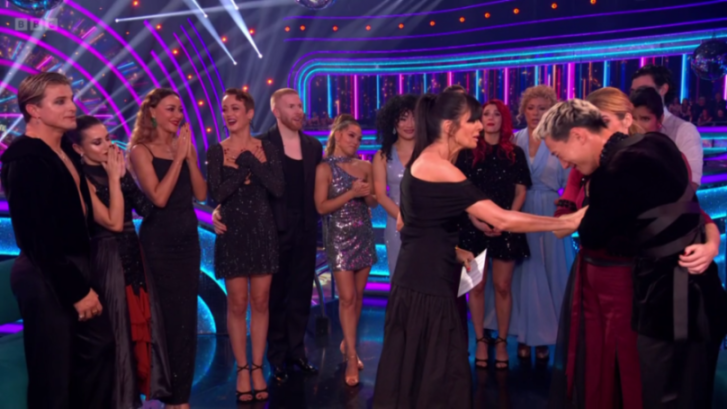 A group of people dressed in formal attire on a brightly lit stage, with one woman comforting another who is crying.