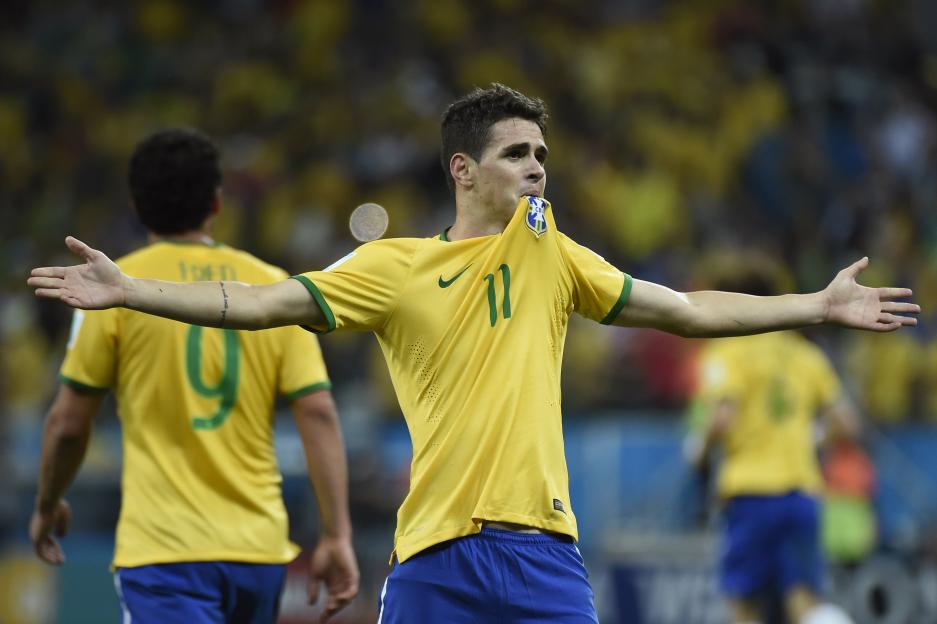 Brazilian midfielder Oscar celebrates a goal with his jersey in his mouth.