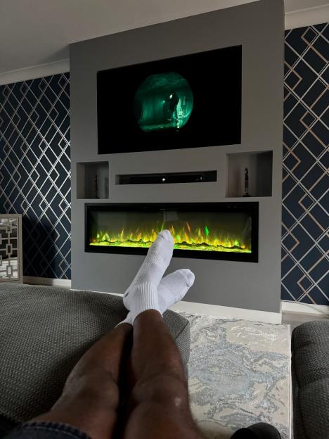 Konnor Ewudzi relaxing with his feet up, watching TV over a fireplace.