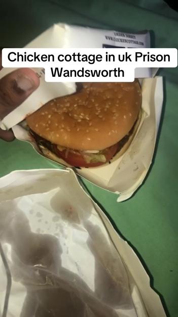 A person holding a burger in a takeaway wrapper, with text overlay "Chicken cottage in uk Prison Wandsworth".