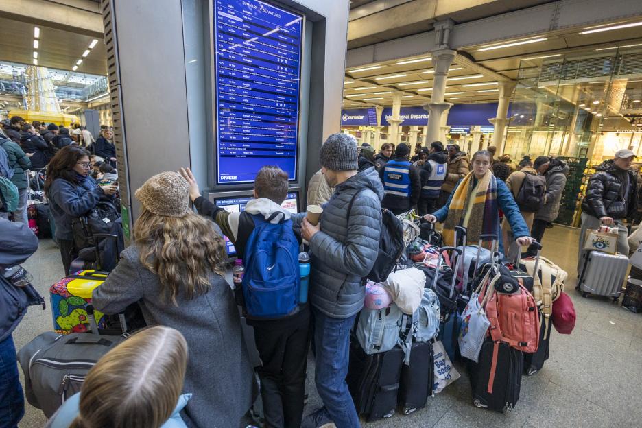 Passengers looking at the departure board at St Pancras Station, with a Eurostar train to Paris Nord listed as "Delayed".