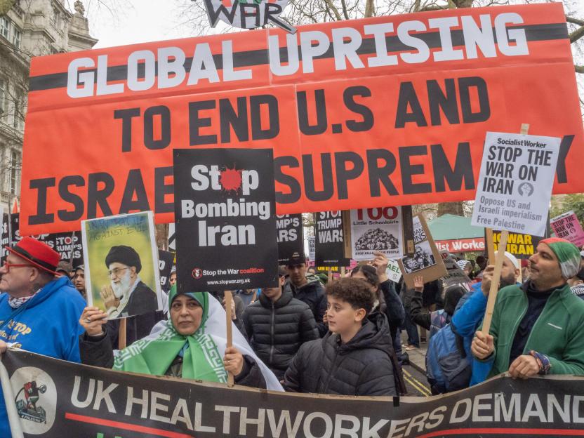 Protestors marching with signs reading "GLOBAL UPRISING TO END U.S. AND ISRAEL SUPREMACY," "Stop Bombing Iran," and "STOP THE WAR ON IRAN."