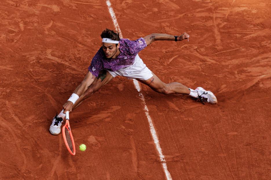 Flavio Cobolli reaching for a tennis ball with his racket during the French Open at Roland Garros.