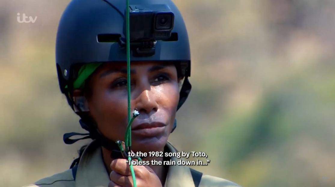 A person wearing a black helmet with a camera attached to it, looking upward, while holding a rope.