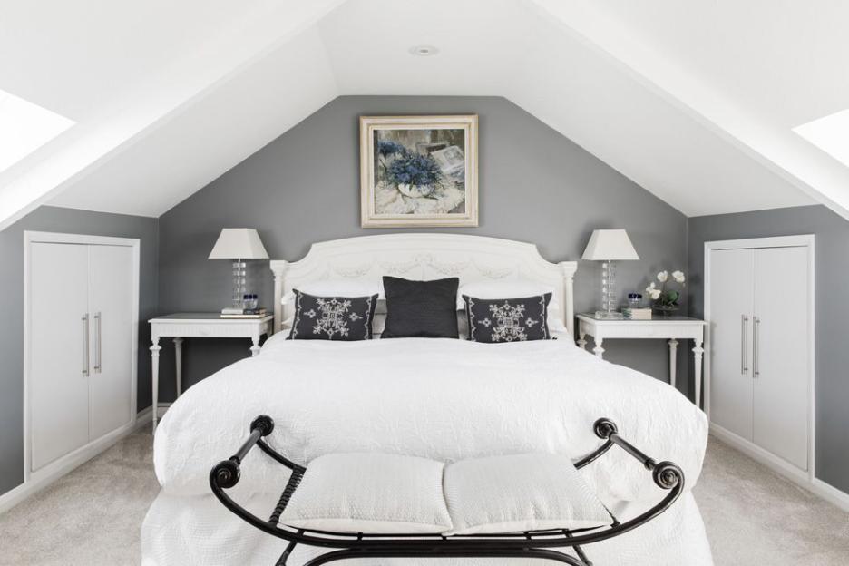 A white bed with white and gray pillows and a black bench in a gray bedroom.