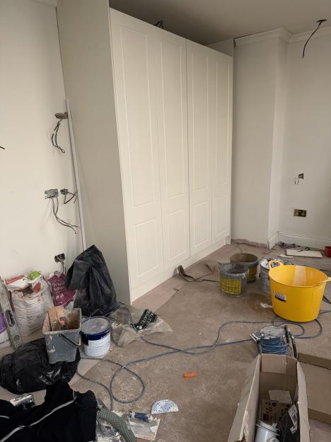 A partially completed room with white fitted wardrobes, exposed wires, building materials, and buckets on the floor.