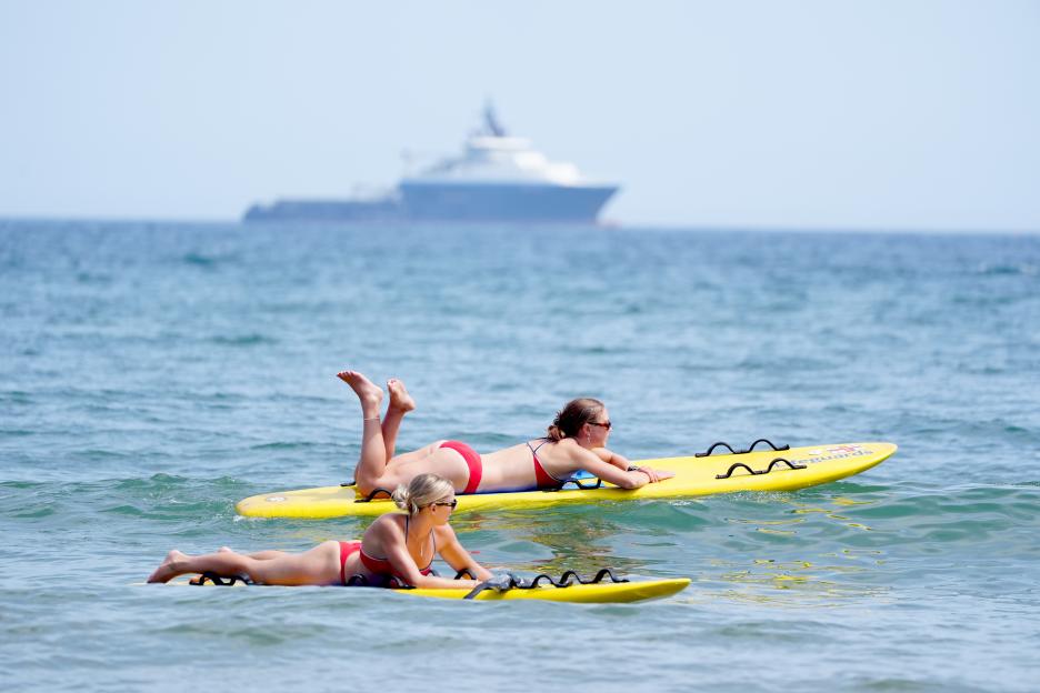 Lifeguards in red bikinis on yellow surfboards monitoring people in the sea.