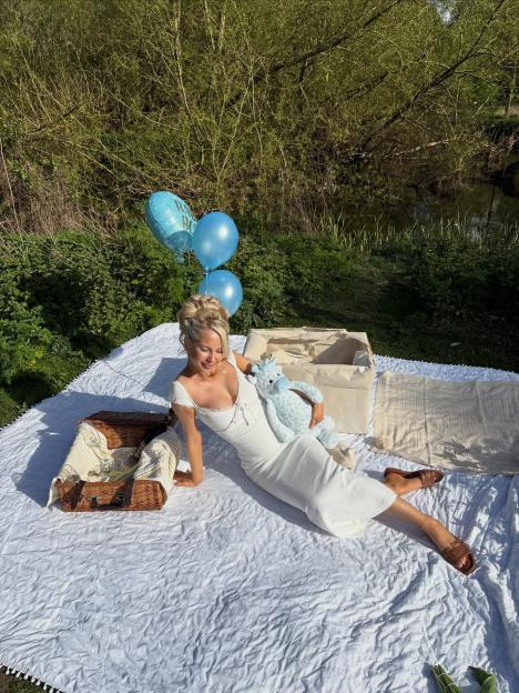 Elsa Rae poses at an outdoor picnic with blue "Baby Boy" balloons and a plush toy.