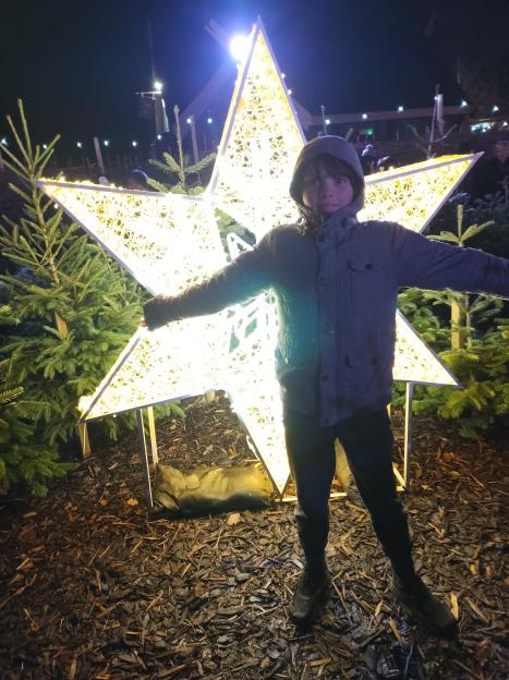 A child in a hooded jacket stands in front of a large, glowing star decoration at Drayton Manor.
