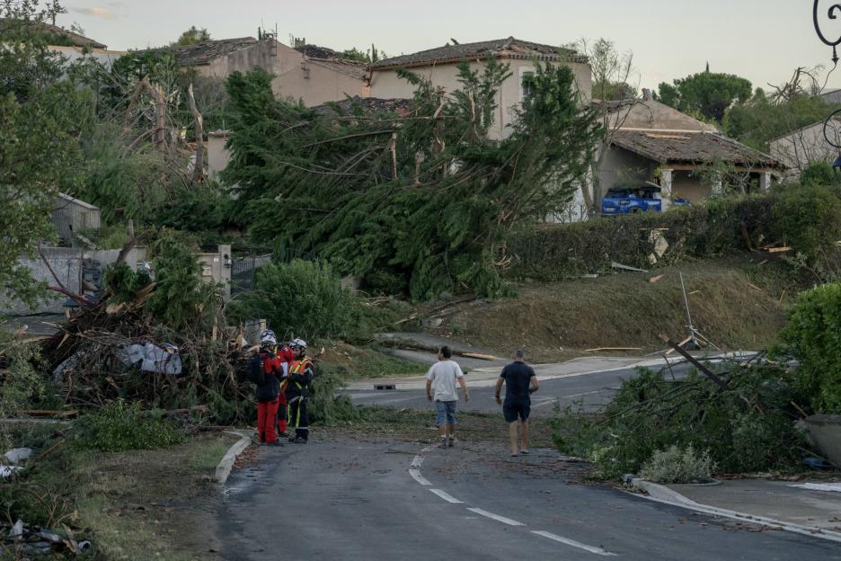 Two men walk past emergency personnel and debris from a tornado.