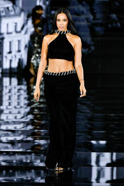 Rochelle Humes walks the runway in a black halter top, matching velvet skirt, and a coiled metallic belt and necklace.