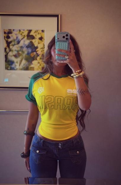 Woman taking a mirror selfie, wearing a yellow Brazil soccer jersey and blue jeans.