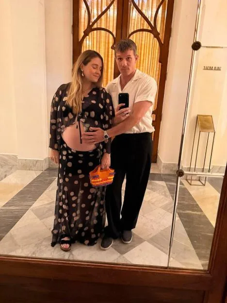 Will Best and Tobi Rose standing in front of a mirror with Tobi placing her hand on her pregnant belly.