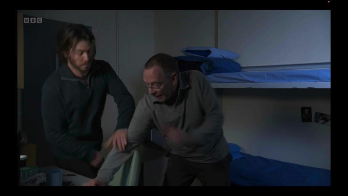 Two men grappling in a prison cell with bunk beds.