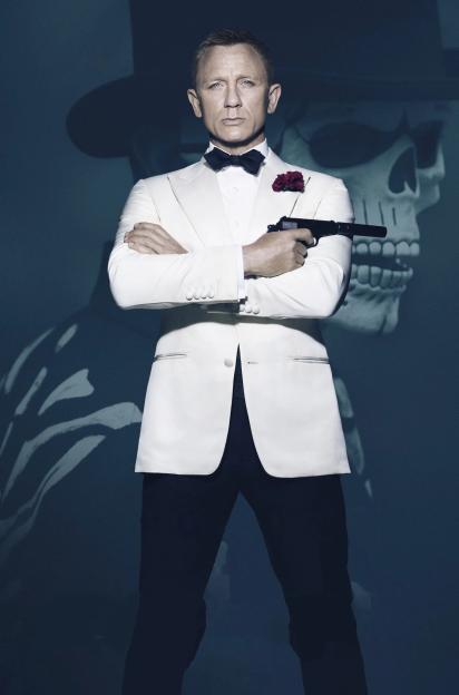 Daniel Craig as James Bond in a white tuxedo, holding a gun with a skull projected behind him, from the film "Spectre."