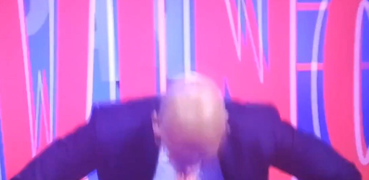 Paolo Di Canio appearing to jump in front of a blue and pink striped background.