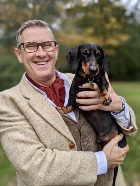 Graeme Hall smiling while holding a dachshund.