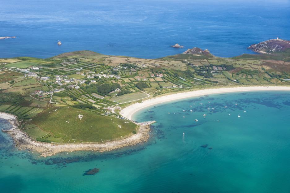 Aerial view of the Isles of Scilly, England, showing coastal towns, beaches, and boats in the turquoise sea.