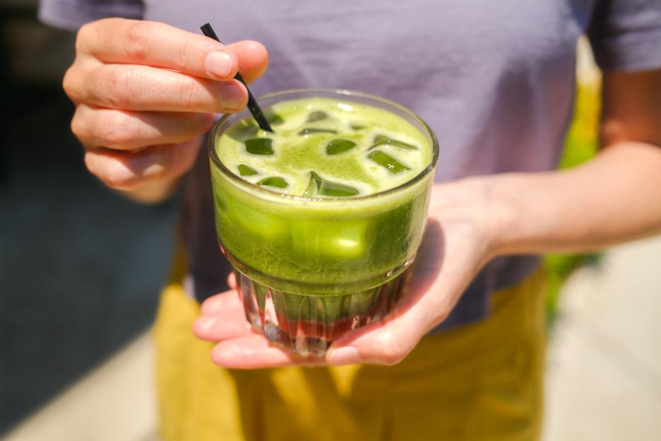 Person stirring iced strawberry matcha drink outdoors