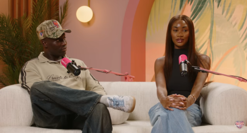 Two podcasters, a man and a woman, seated on a white sofa.
