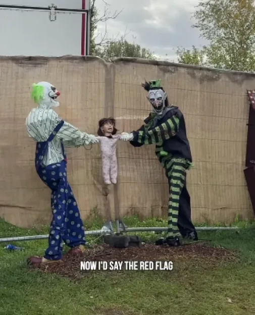 Two creepy clown decorations holding up a doll in a field at the Suffolk Pumpkin Patch.