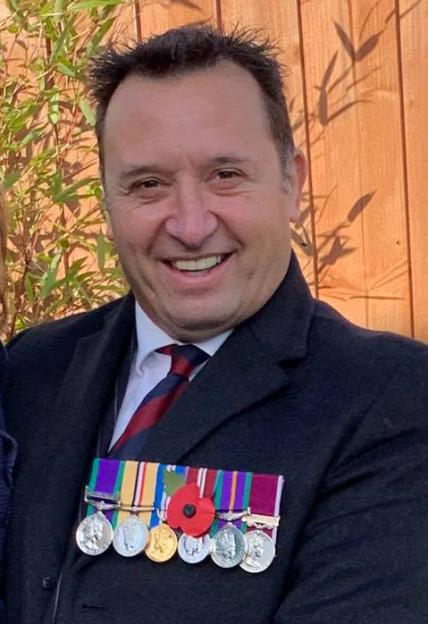 Gareth Lloyd, a man in a suit and tie, smiling, with military medals pinned to his chest.