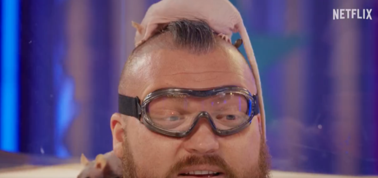 A man wearing safety goggles with a rat on his head.