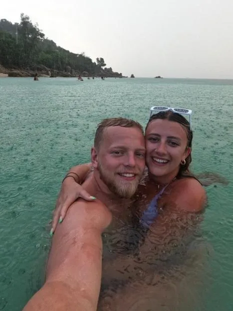 A smiling young couple hugging and posing for a selfie while swimming in the sea in the rain.