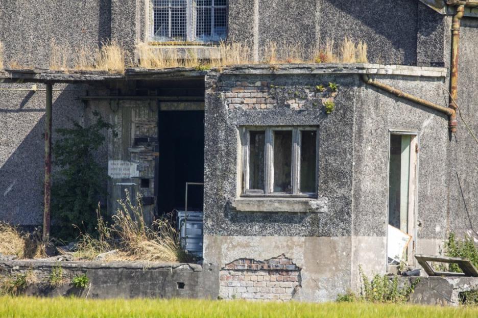 One of the last surviving World War I naval bomb depots, a dilapidated building with crumbling walls, overgrown vegetation, and broken windows.