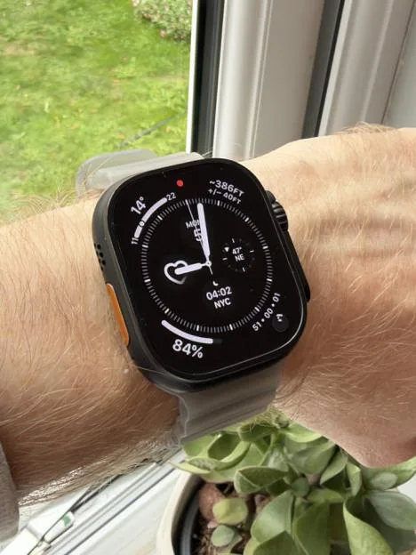 An Apple Watch Ultra on a person's wrist, displaying an analog watch face with complications including a heart rate monitor, battery percentage, elevation, and time in New York City.