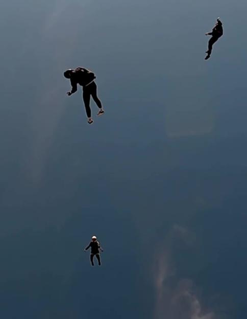 Three skydivers fall through the sky, one in the distance and two closer.