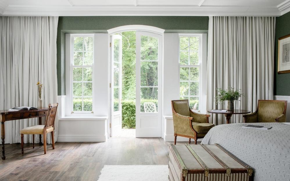 A bedroom with dark green walls, white trim, and a large open doorway leading to an outdoor garden.