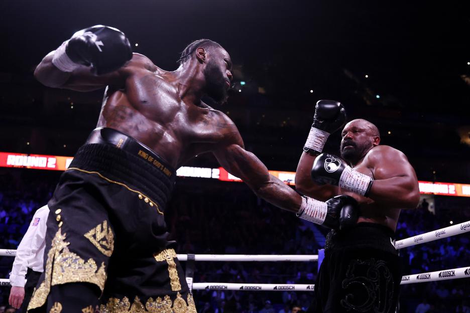 Deontay Wilder throwing a punch at Derek Chisora during a boxing match.