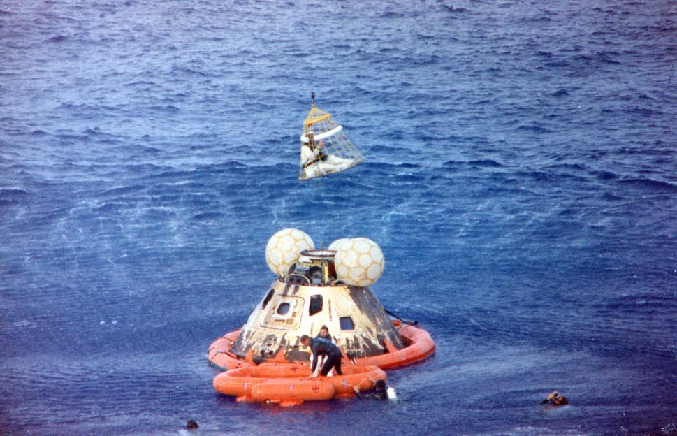 Apollo 13 astronaut Jack Swigert is hoisted from the command module in a net, while Jim Lovell and Navy swimmers await recovery in the Pacific Ocean.