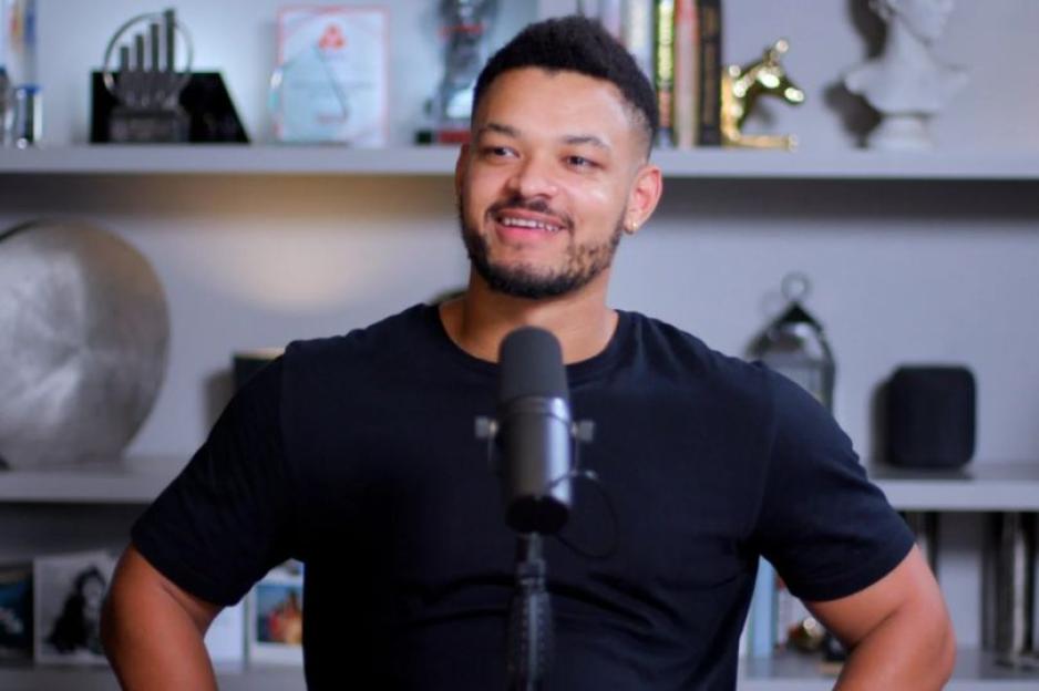 Steven Bartlett of Diary of a CEO podcast in a black t-shirt, standing behind a microphone.