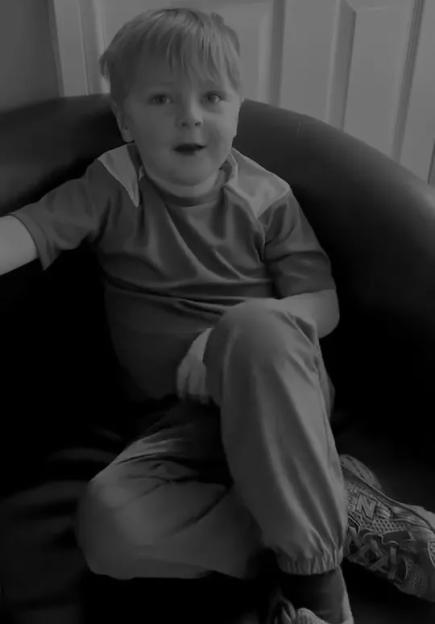 A young boy sitting in a chair, looking forward with a surprised expression.