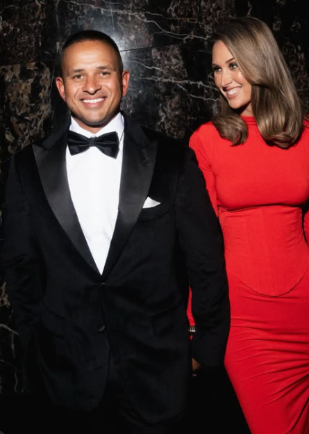 Man in a tuxedo and woman in a red dress smiling.