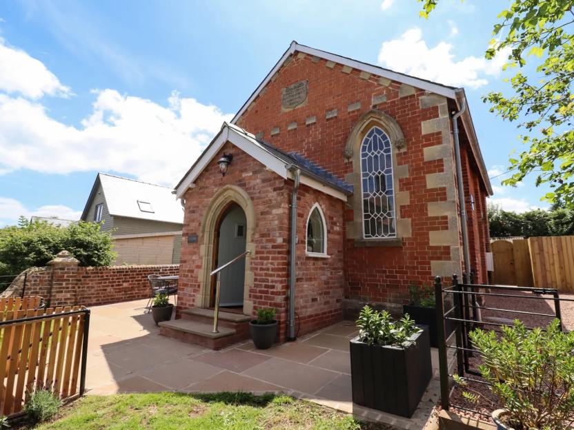 The Old Chapel, a red brick cottage with an arched doorway and tall arched window, with a patio and garden space.