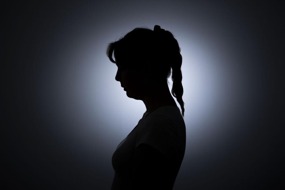 Photo illustration of the silhouette of a young woman standing against a white wall, symbolizing loneliness.
