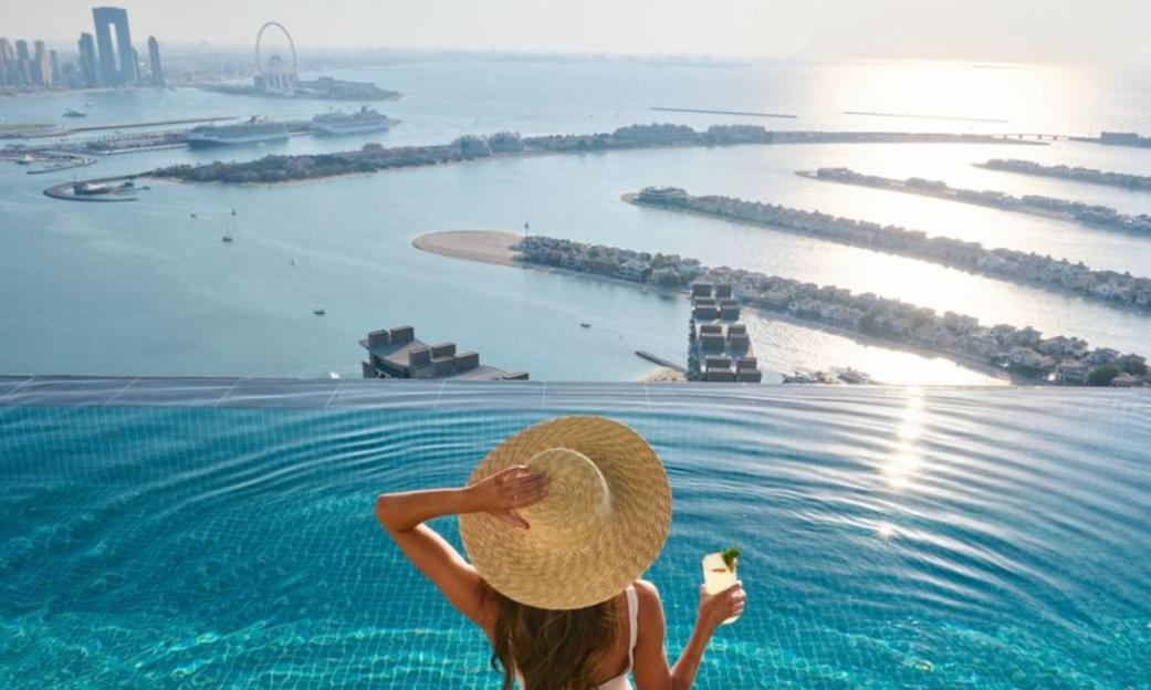 A person in a straw hat enjoys a drink in the Aura Sky Pool overlooking Dubai's Palm Jumeirah.