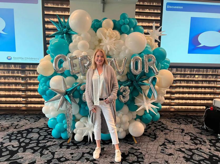 Eileen McGill Fox in front of a balloon display spelling "CERVIVOR" in teal, white, and silver.
