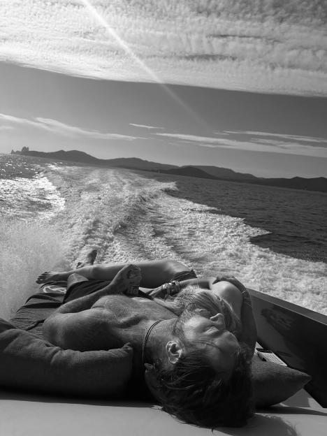 A couple lounge on the back of a boat as it speeds through the water, leaving a wake behind them.