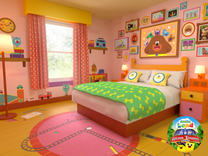 Illustration of a Hey Duggee-themed hotel room with pink walls, a large bed with a green blanket, and Hey Duggee art on the walls.