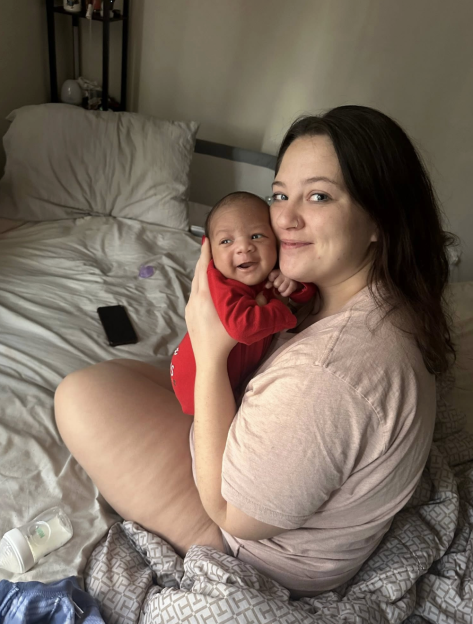 A woman holding a baby in a red outfit on a bed.