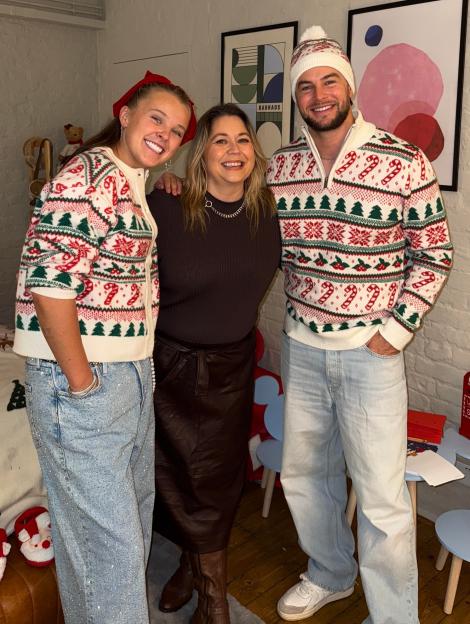Three people wearing Christmas-themed sweaters are smiling at the camera.
